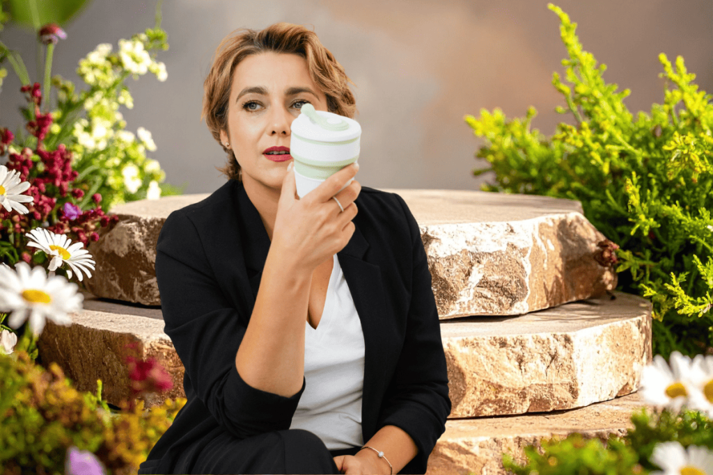 Confident midlife woman in a black blazer enjoying a coffee break in a lush garden, representing a calm, consistent skin care routine for women over 50