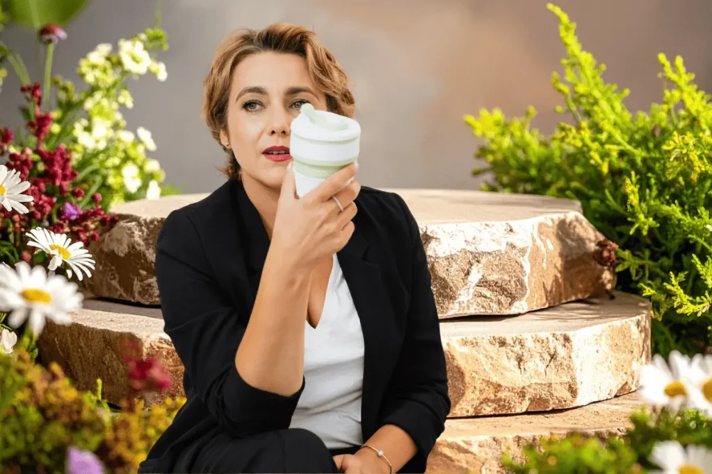 Confident midlife woman in a black blazer enjoying a coffee break in a lush garden, representing a calm, consistent skin care routine for women over 50