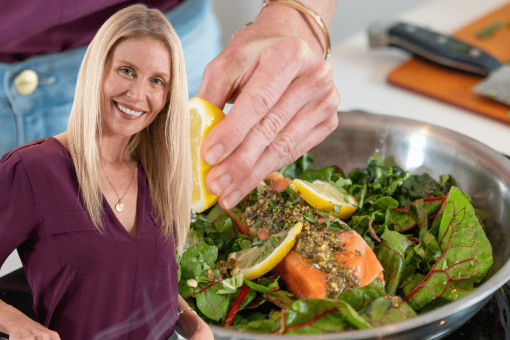 Smiling woman cooking a healthy meal with salmon and greens, highlighting nutritious foods rich in vitamin D and calcium.