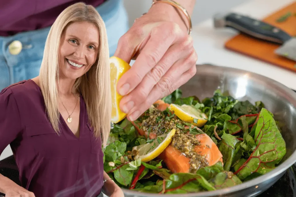 Smiling woman cooking a healthy meal with salmon and greens, highlighting nutritious foods rich in vitamin D and calcium.