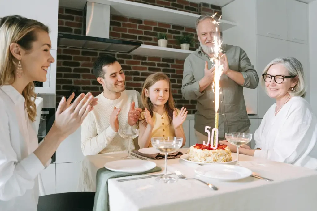 Family celebrating a woman’s 50th birthday around a dinner table with a cake and sparkling candle, symbolizing joyful, connected healthy aging.