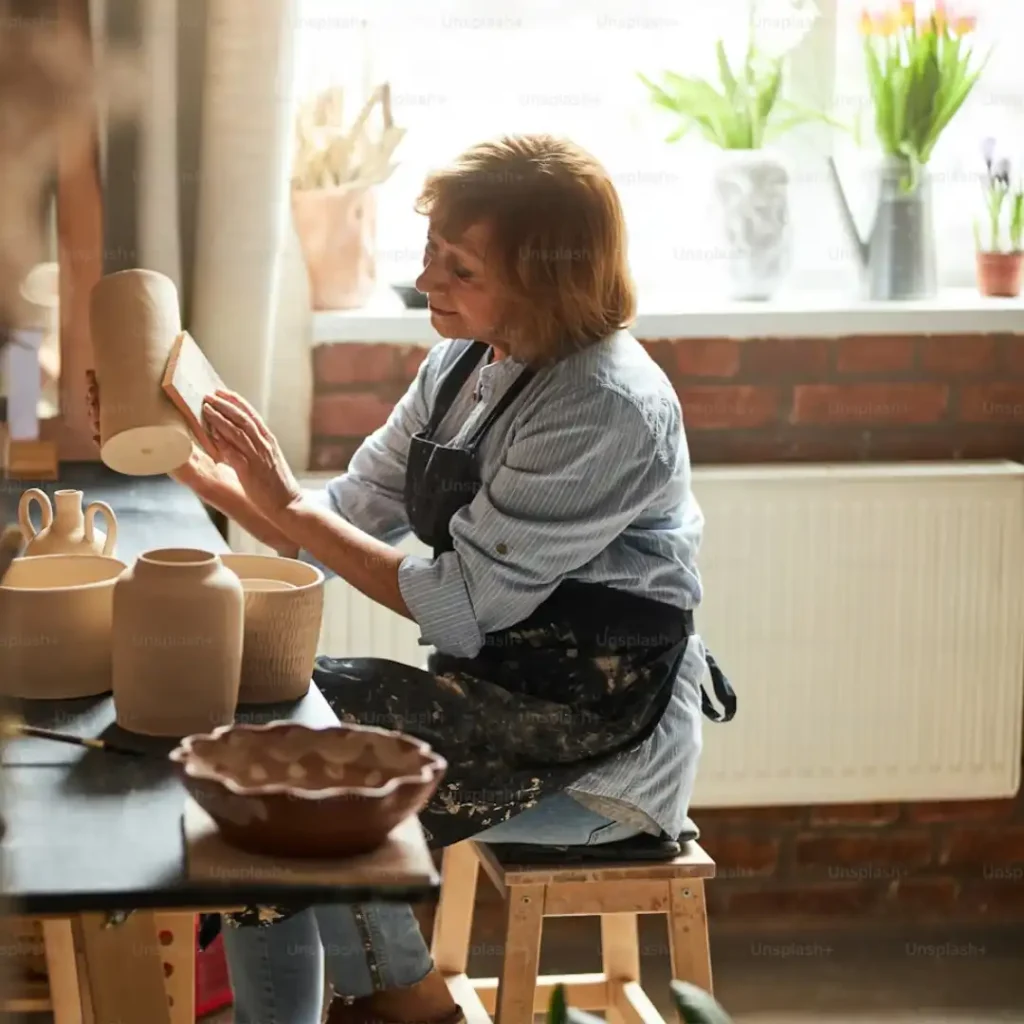 Woman over 50 deeply engaged in a meaningful creative pottery practice in a calm, sunlit workshop.