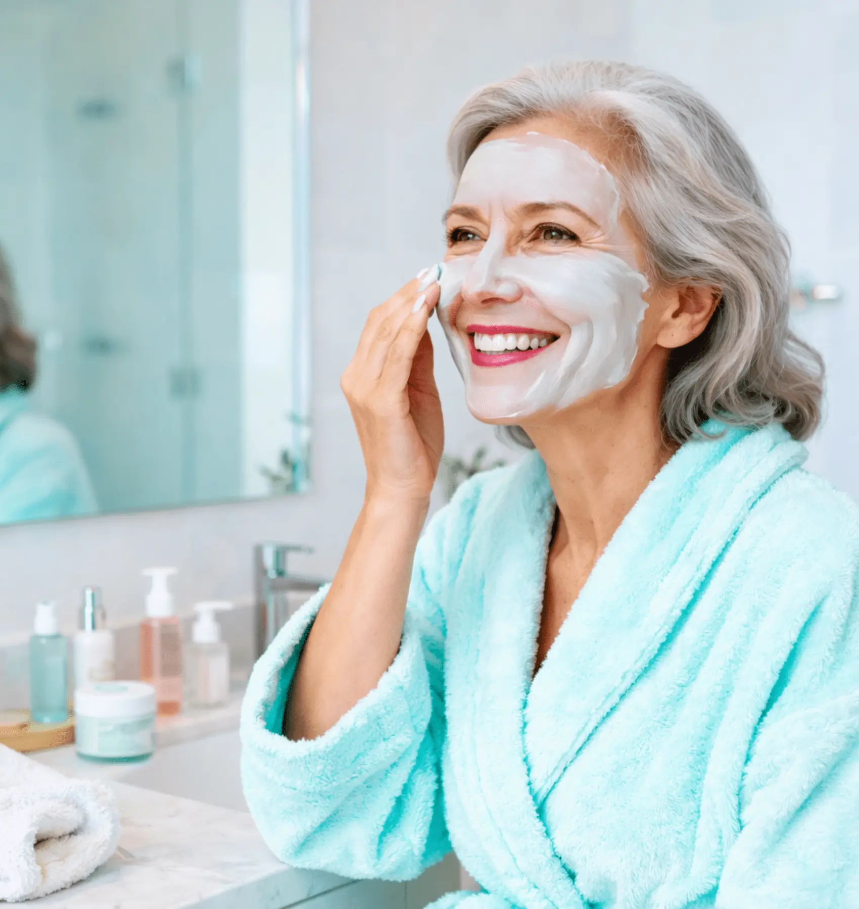 Smiling mature woman applying a facial mask in a bright bathroom, symbolizing skincare, self-care, and beauty for women over 50
